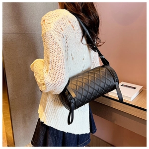 Detail view of the black quilted cylinder crossbody bag on model in a modern room