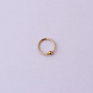 Détail de l'anneau de piercing en acier C avec zircons pavés et breloque boule dorée