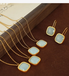 Detailed set of gold necklaces and earrings with square light blue gemstones on wood