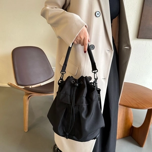 Détail du sac seau noir en nylon avec cordon, porté par un mannequin en manteau beige