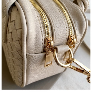 Detail of beige woven handbag showing dual gold zippers and metallic strap buckles