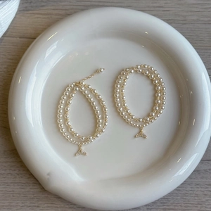 Detail view of double-layer pearl bracelet with zircon fishtail pendant on ceramic tray