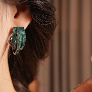 Macro detail of multilayer C-shaped earrings with sparkling green cubic zirconia stones
