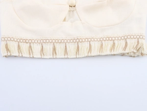 Detailed view of cream-colored linen top featuring tassel hem and woven texture fabric
