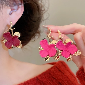 Detail of burgundy floral drop earrings with gold-tone branches worn by a model