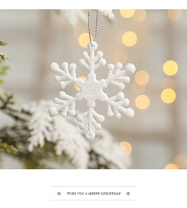 Close-up of a white frosted snowflake ornament hanging on a Christmas tree with golden bokeh