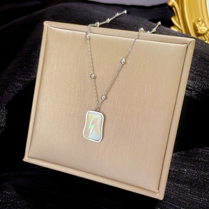 Macro detail of a silver-tone chain necklace with an iridescent rainbow shell pendant