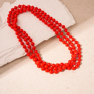 Close-up of three-layer red pearl bead necklace on a white textured stone background