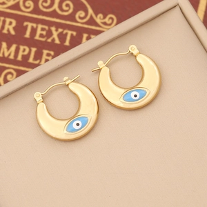 Gold U-shaped Evil Eye earrings with blue enamel center on a textured background