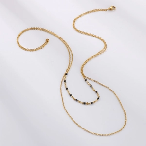 Détail d'un collier double épaisseur doré avec perles minimalistes en résine noire sur la chaîne