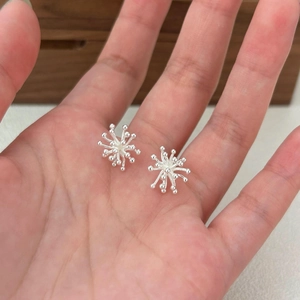 Macro shot of silver radial fireworks stud earrings held in hand for scale