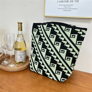 Close-up of a black and green geometric knit tote bag placed on a rustic wooden table