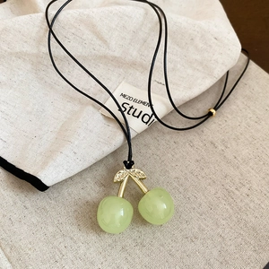Macro shot of light green resin cherry pendant with golden metal leaves on black cord