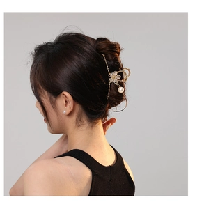 Detailed view of a gold flower hair claw clip with rhinestones and a pearl pendant on hair