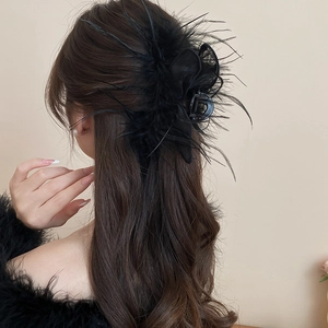 Macro view of black feather hair claw clip on model's wavy hair for elegant hairstyle