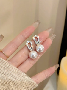 Macro shot of horseshoe-shaped pearl earrings with cubic zirconia inlay on silver metal