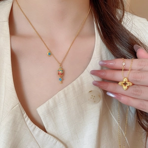 Detail showing gold enamel cylinder pendant and zircon clover necklace on a model