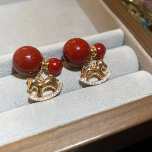 Detailed macro of golden rocking horse earrings with red beads and micro-set diamonds