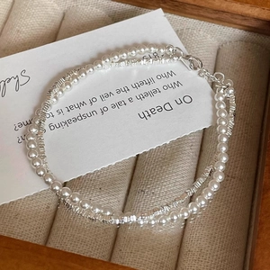 Double-layer bracelet featuring white pearls and silver beaded chain on beige cushion
