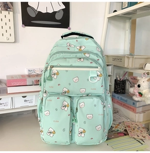 Detail of mint green school backpack with cute white bear and cherry prints on a desk