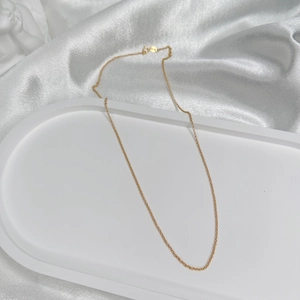 Detail of a thin gold-plated S925 silver O-chain necklace on a white ceramic display tray