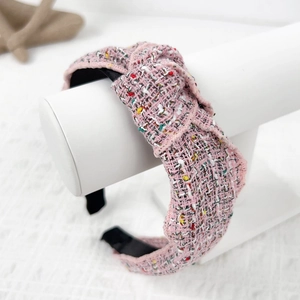 Pink tweed knotted headband with woven texture displayed on a professional white stand