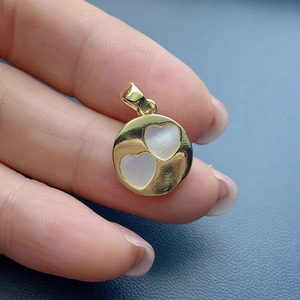 Macro shot of a round gold pendant featuring two white mother-of-pearl heart inlays