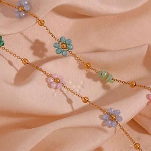 Detail of colorful crystal flower beads on a thin gold chain against beige silk