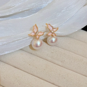 Vue macro de boucles d'oreilles papillon en émail rose avec perles blanches et doré