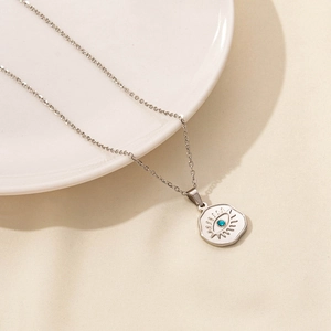 Macro view of evil eye pendant with blue gemstone on silver chain over white ceramic plate
