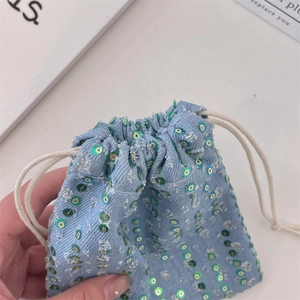Detail of light blue denim drawstring pouch with green and gold sequins and white rope