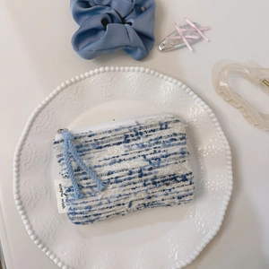Primo piano di mini pochette in tweed blu e bianco con etichetta su piatto in ceramica