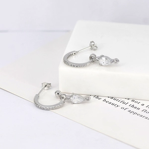 Macro detail of silver teardrop earrings with pavé crystals on white stone pedestal