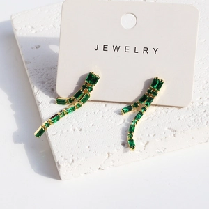 Detail of emerald zircon tassel earrings on a display card with elegant shadow lighting