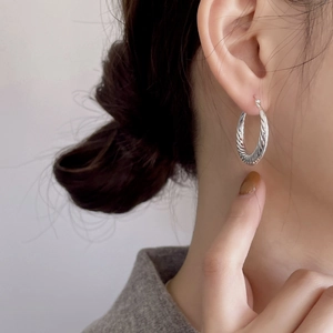 Minimalist 925 sterling silver hoop earrings with twisted wave design worn by a model