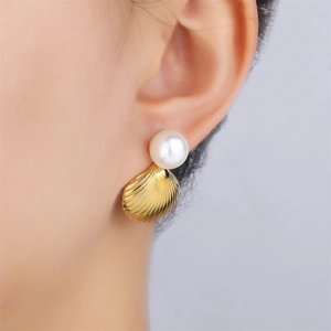 Close-up of elegant gold shell-shaped earring with a large white pearl on a model