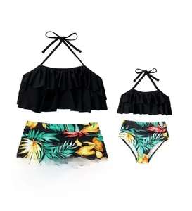 Flat lay of mommy and me matching tankini sets with black ruffle tops and tropical leaf prints