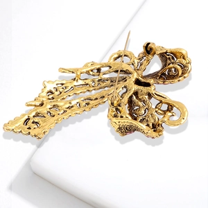Vintage gold bow brooch with rhinestone details and filigree pattern on white background