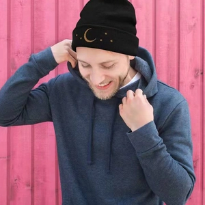 Close-up of gold star and moon embroidery on a black ribbed knit beanie hat