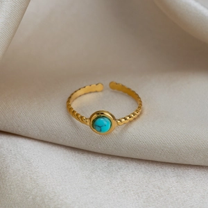 Détail d'une bague bohème dorée avec pierre turquoise et anneau à motif torsadé