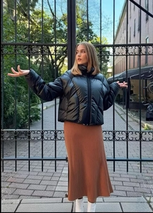 Glossy black quilted puffer jacket styled with a brown knit skirt and white boots