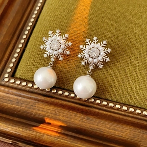 Détail de boucle d'oreille flocon argenté avec cristaux et grande perle blanche