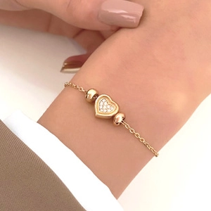 Detail of a gold bracelet with a heart pendant and pavé crystals on a model's wrist
