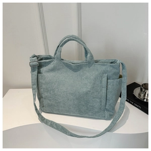 Light blue corduroy tote bag with adjustable strap and handles on a white tabletop