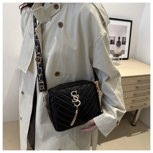 Detail of black quilted crossbody bag with golden S-buckle, fringe charm and woven strap