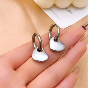 Polished silver heart pendant hoop earrings held by hand for scale and modern style