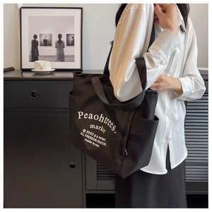 Detail of a black canvas tote bag with white lettering and a practical side pocket