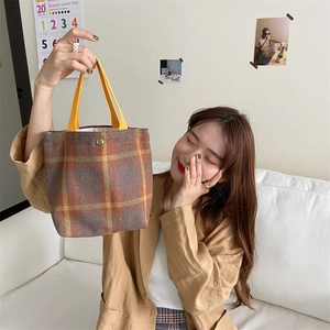 Detail of retro woolen plaid tote bag with warm orange handles and bronze metal snap button