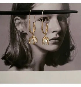 Detail von eleganten Goldohrringen mit weißen Perlen an einem minimalistischen Ständer