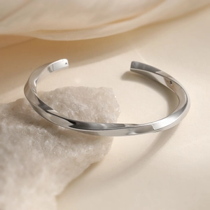 Polished silver geometric twist cuff bracelet on natural stone with a mirror finish